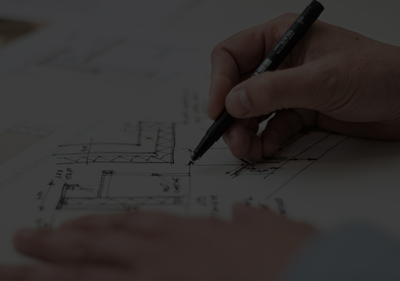 A dark close-up of somebody drawing on a piece of paper with building-related drawings.