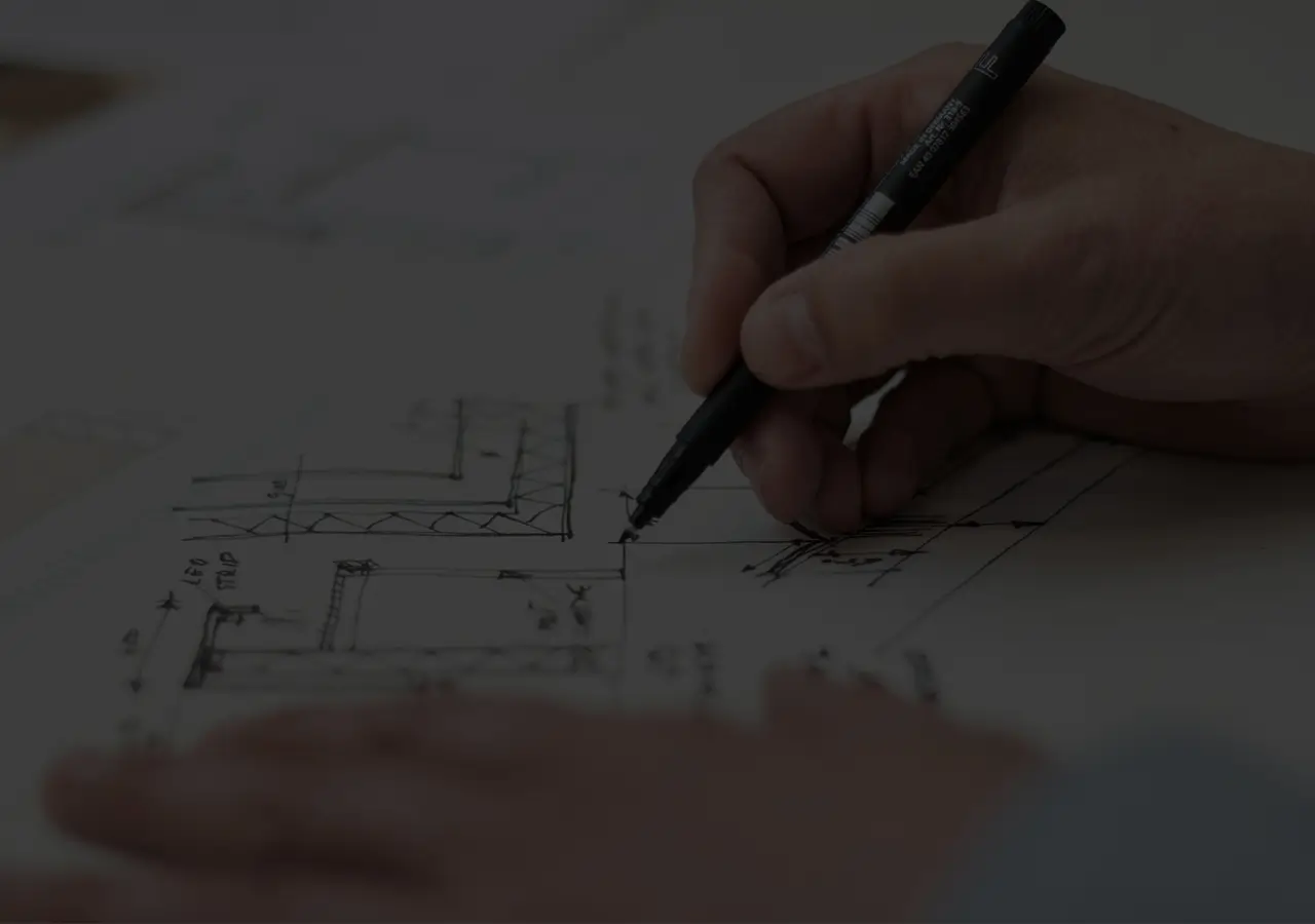 A dark close-up of somebody drawing on a piece of paper with building-related drawings.