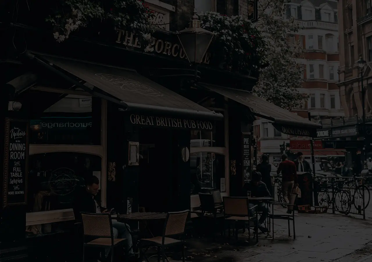 A black-and-cream-themed London pub with a sign reading 'Great British Pub Food', and people sitting and passing outside.