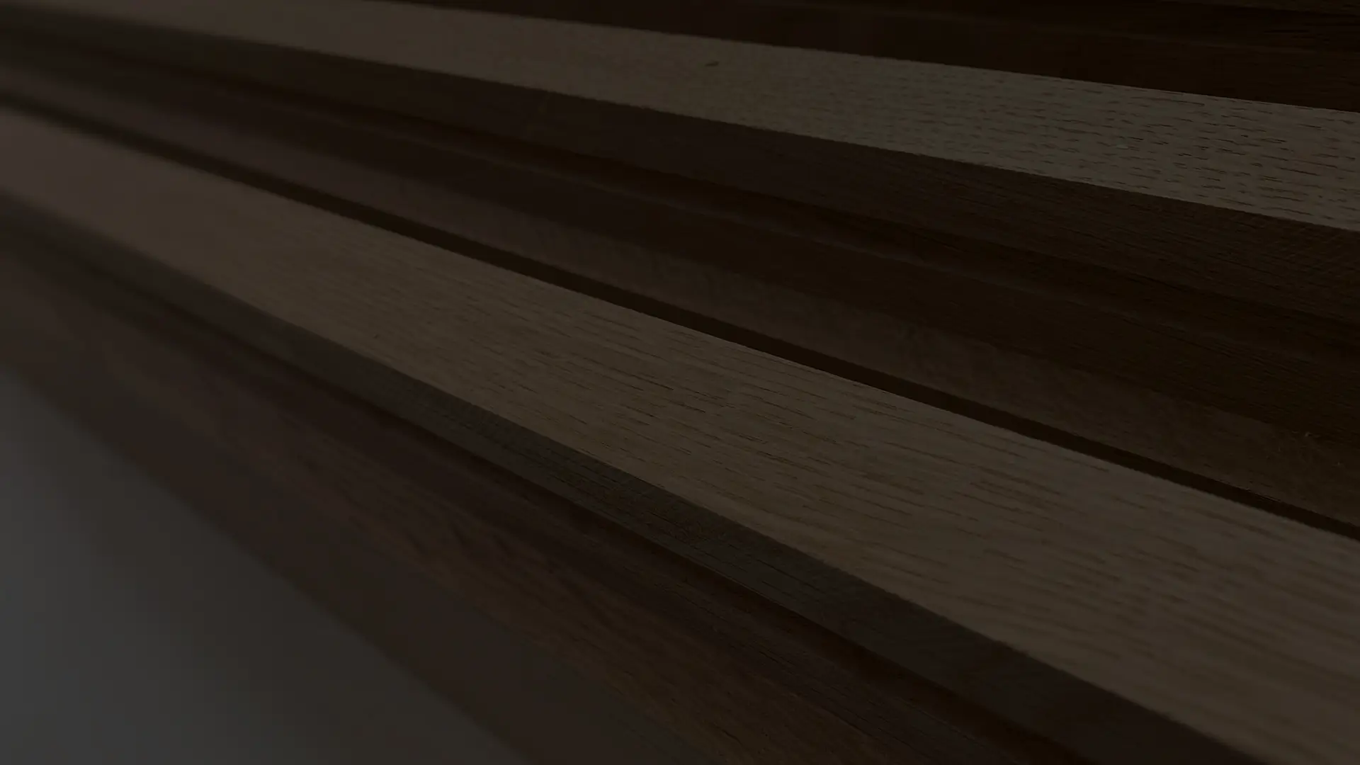 A dark sideways close-up of smooth machined pieces of oak timber on a table in the malek joinery workshop.