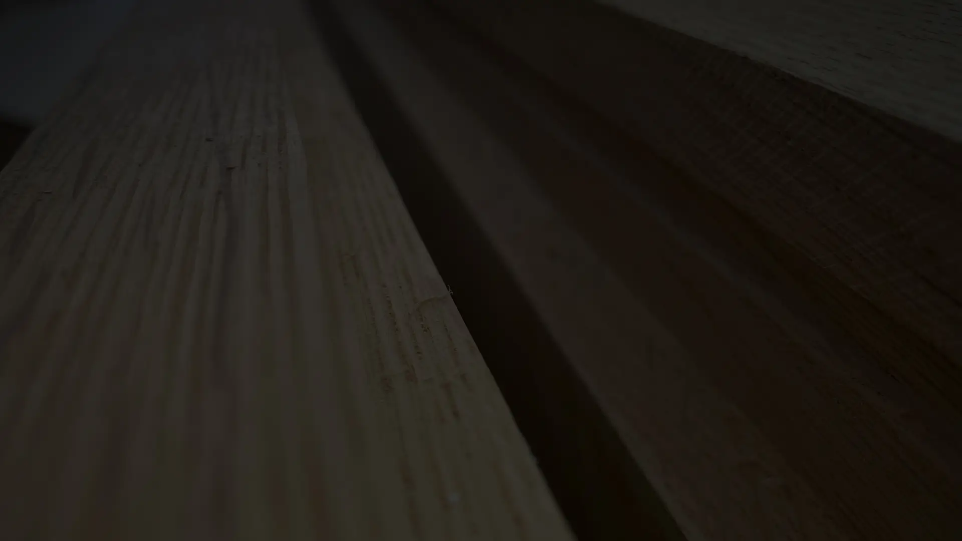 A dark straight-on close-up of smooth machined pieces of oak timber on a table with small imperfections in the malek joinery workshop.