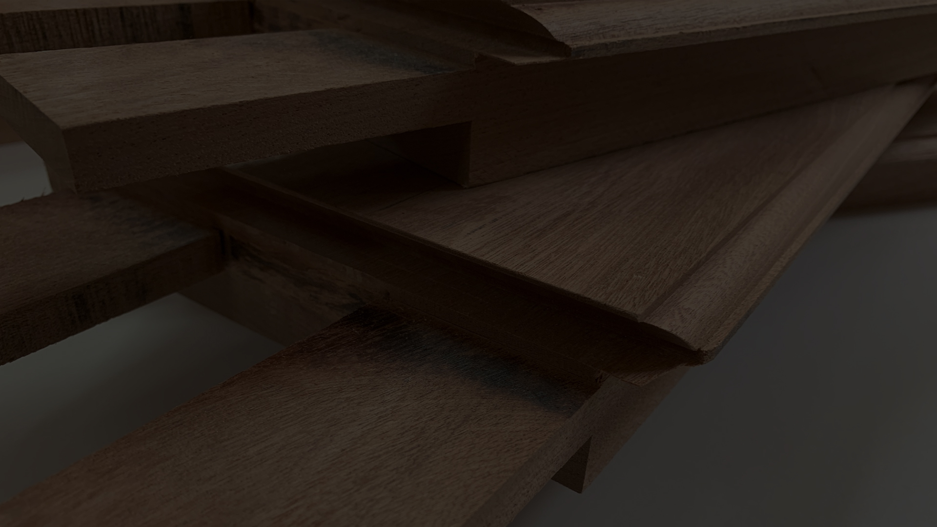 A dark close shot of multiple pieces of machined meranti timber with tenon joints stacked on top of one another.
