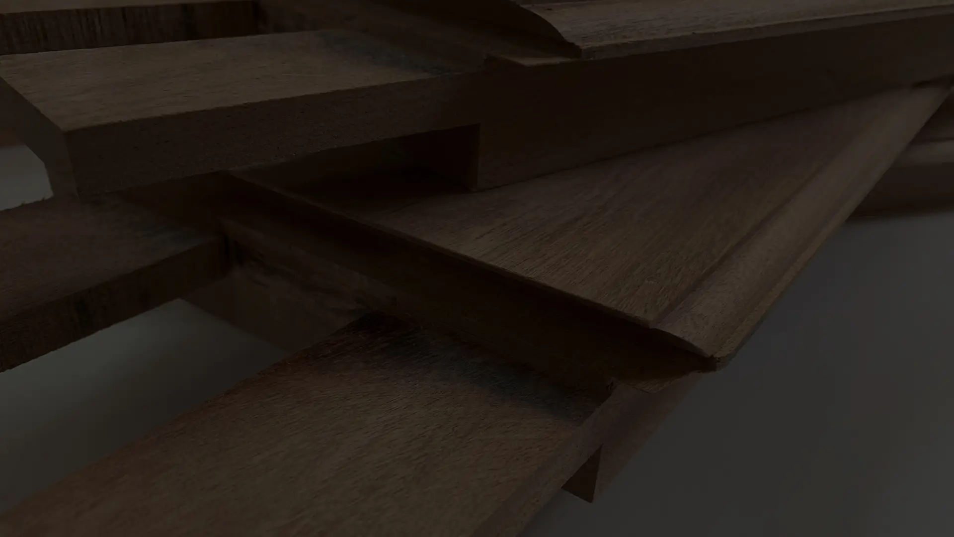 A dark close shot of multiple pieces of machined meranti timber with tenon joints stacked on top of one another.