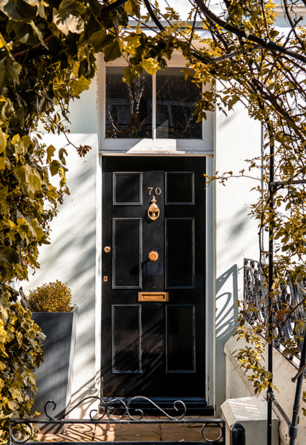 A Georgian-style timber black fanlight door, in a nature-focussed front yard, with polished brass fittings and the number 70.