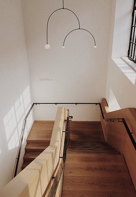 A contemporary timber staircase with a 180-degree turn and thin black metal handrailings, in a tall space with white walls, a modern light fitting, a window to the right, and the sun shining in.