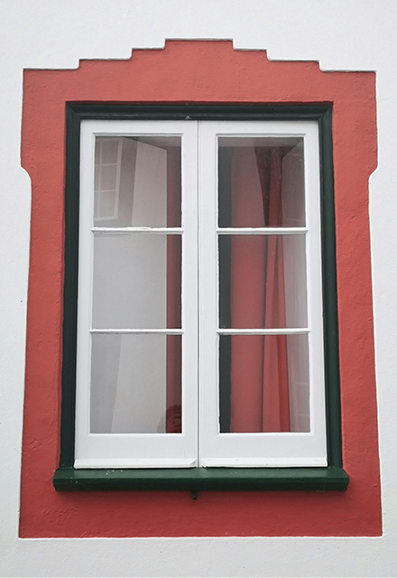 A timber storm casement window with a black frame and sill, sitting in a red-painted part of a mostly white wall.